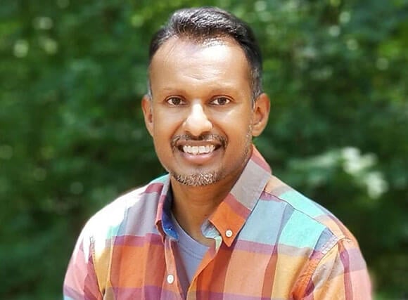 Nicholas Isaac smiles at the camera in a plaid shirt