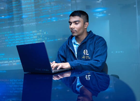 Student typing on a laptop in a blue classroom